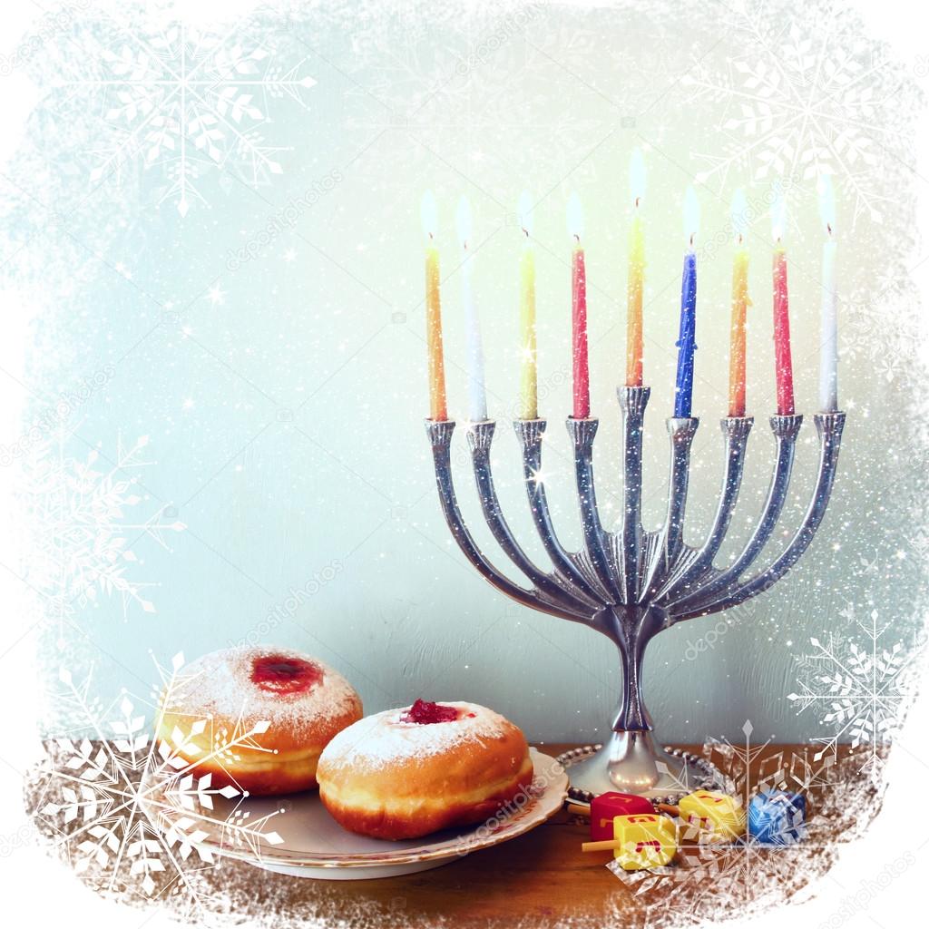 image of jewish holiday Hanukkah with menorah (traditional Candelabra), donuts and wooden dreidels (spinning top). retro filtered image with glitter and snowflakes overlay.