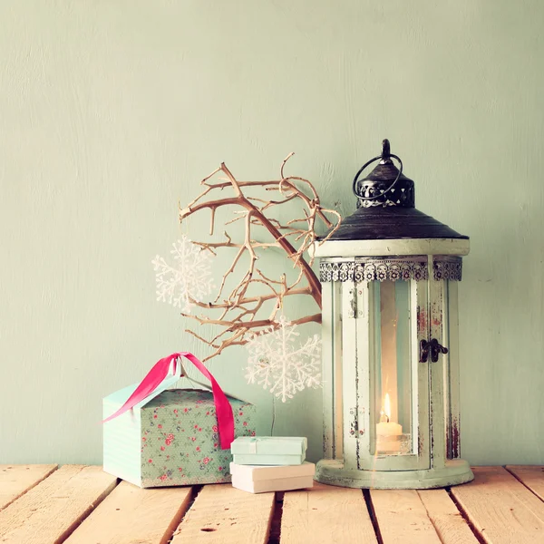 White wooden vintage lantern with burning candle, christmas gifts and tree branches on wooden table. retro filtered image. — Stock Photo, Image