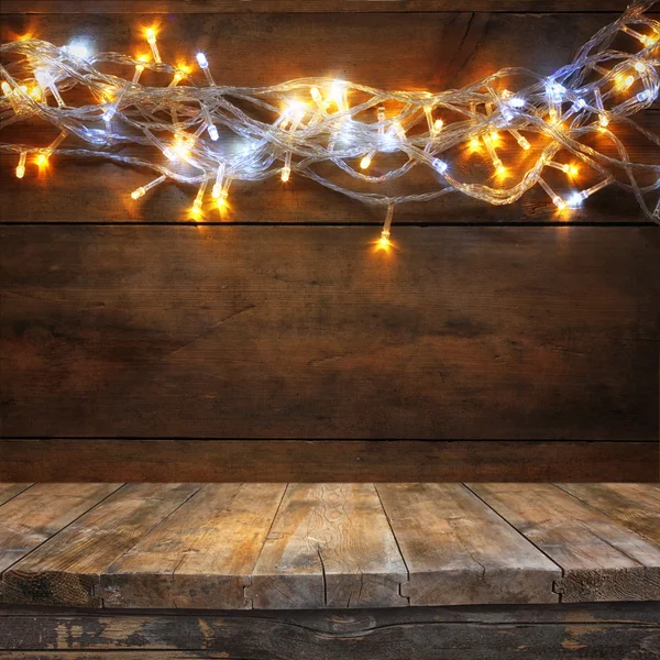 Mesa de madera frente a luces de guirnalda de oro caliente de Navidad sobre fondo rústico de madera. imagen filtrada. enfoque selectivo . — Foto de Stock