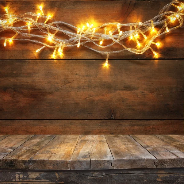 Wood board table in front of Christmas warm gold garland lights on wooden rustic background. filtered image. selective focus. — Stock Photo, Image