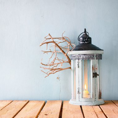 white wooden vintage lantern with burning candle and tree branches on wooden table.