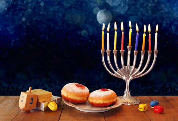 Low key image of jewish holiday Hanukkah with menorah, doughnuts and wooden dreidels (spinning top). retro filtered image. — Stockfoto