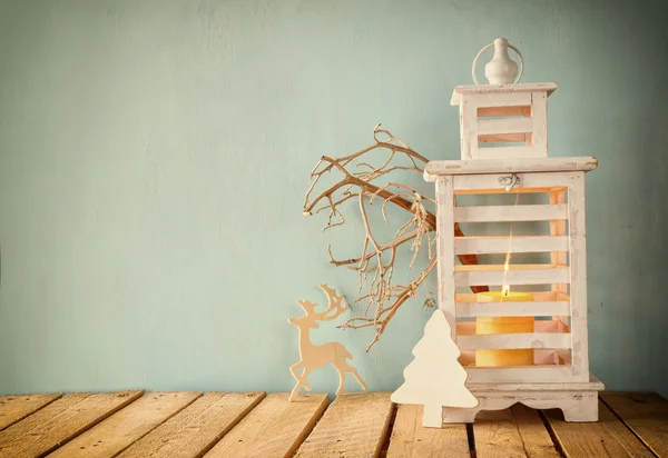 Lanterna vintage de madeira branca com vela ardente, veados de madeira, presentes de Natal e galhos de árvore na mesa de madeira. retro filtrado . — Fotografia de Stock