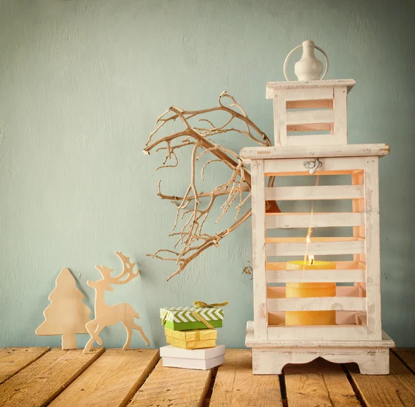 White wooden vintage lantern with burning candle, wooden deer, christmas gifts and tree branches on wooden table. retro filtered image. — Φωτογραφία Αρχείου