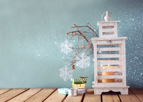 White wooden vintage lantern with burning candle christmas gifts and tree branches on wooden table. retro filtered image. — Stockfoto