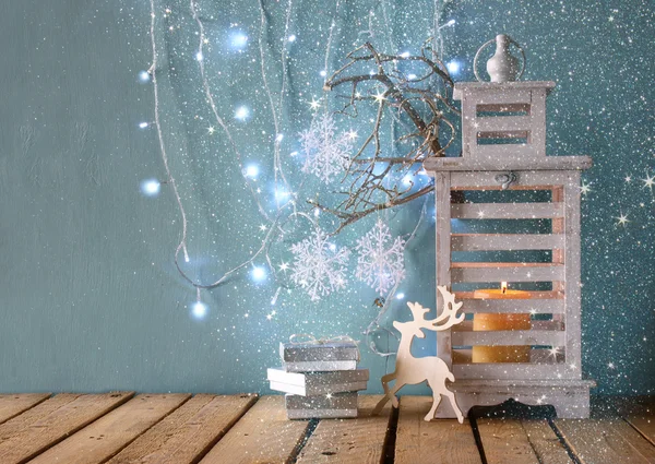 Linterna vintage de madera blanca con vela encendida, ciervos de madera, regalos de Navidad y ramas de árbol en la mesa de madera. imagen filtrada retro . — Foto de Stock
