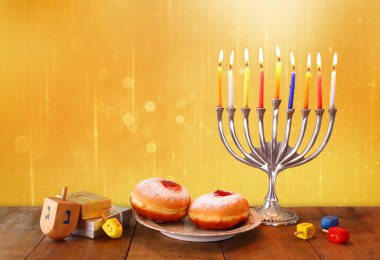 low key image of jewish holiday Hanukkah with menorah, doughnuts and wooden dreidels (spinning top). retro filtered image. clipart