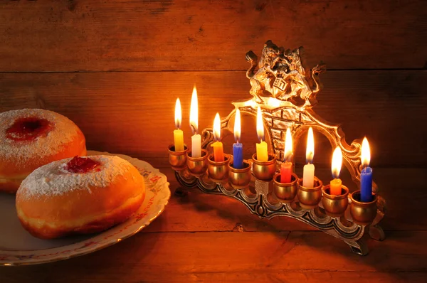 Low key image of jewish holiday Hanukkah with menorah (traditional Candelabra), donuts and wooden dreidels (spinning top). — Stock Photo, Image