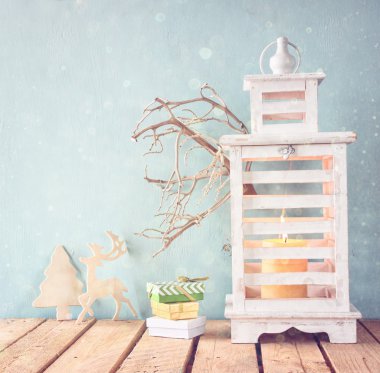 Beyaz ahşap vintage fener mum, ahşap geyik, Noel hediyeleri ve ağaç dalları üzerinde ahşap masa yanma ile. glitter kaplaması ile Retro filtre uygulanmış görüntü.