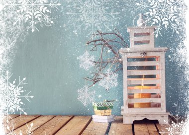 white wooden vintage lantern with burning candle, christmas gifts and tree branches on wooden table. retro filtered image.