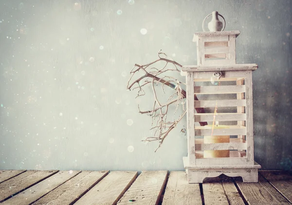 White wooden vintage lantern with burning candle and tree branches on wooden table. retro filtered image with glitter overlay. — Stock Photo, Image