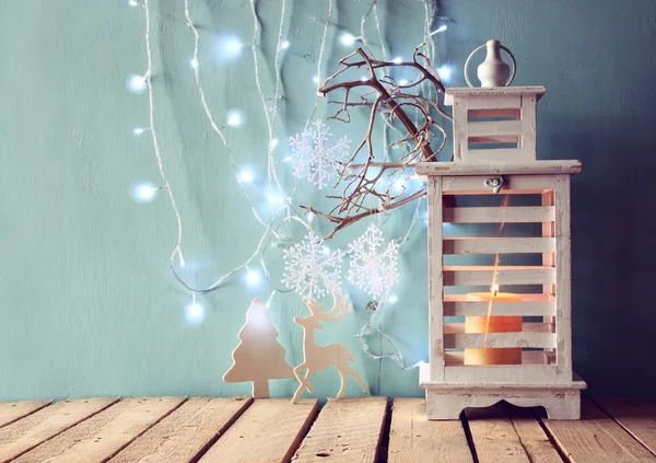 White wooden vintage lantern with burning candle, wooden deer, christmas gifts and tree branches on wooden table. retro filtered image. — 스톡 사진