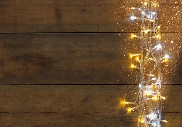 Christmas warm gold garland lights on wooden rustic background. filtered image with glitter overlay.