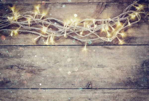 Christmas warm gold garland lights on wooden rustic background. filtered image with glitter overlay. — Stockfoto