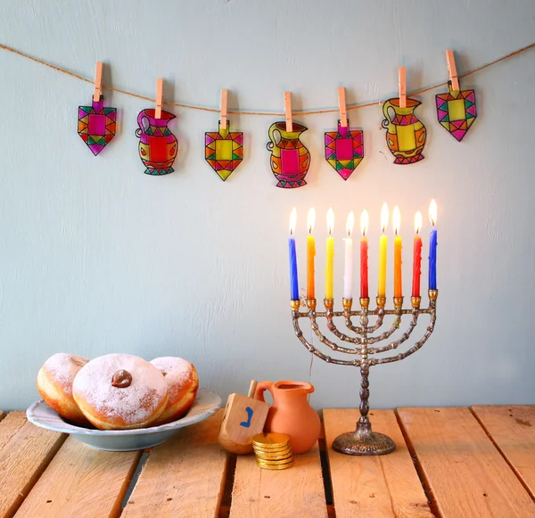 Image of jewish holiday Hanukkah with menorah (traditional Candelabra), donuts and wooden dreidels (spinning top). glitter background. — Stockfoto
