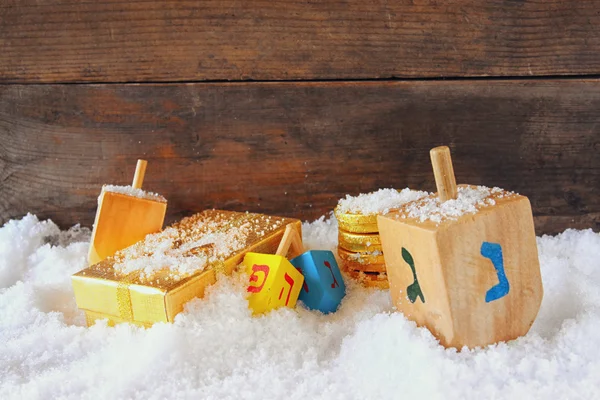 image of jewish holiday Hanukkah with wooden colorful dreidels (spinning top) and chocolate traditional coins over december snow.