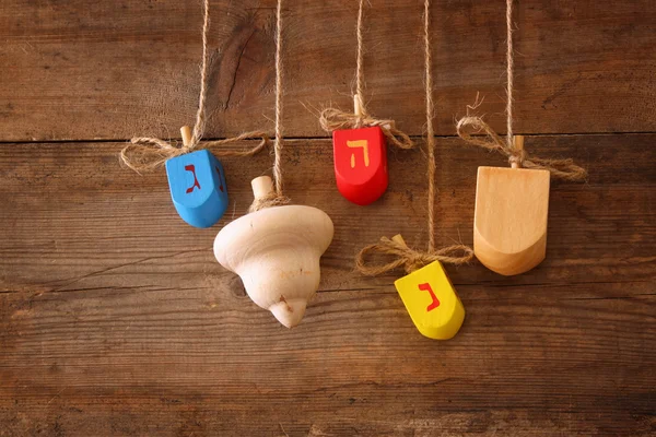 Image of jewish holiday Hanukkah with wooden colorful dreidels (spinning top) hanging on a rope over wooden background. — ストック写真