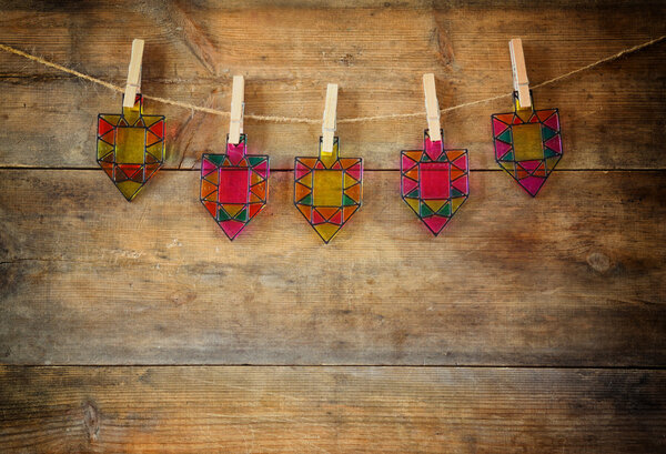 image of jewish holiday Hanukkah with Stained-glass colorful dreidels (spinning top) hanging on a rope over wooden background.