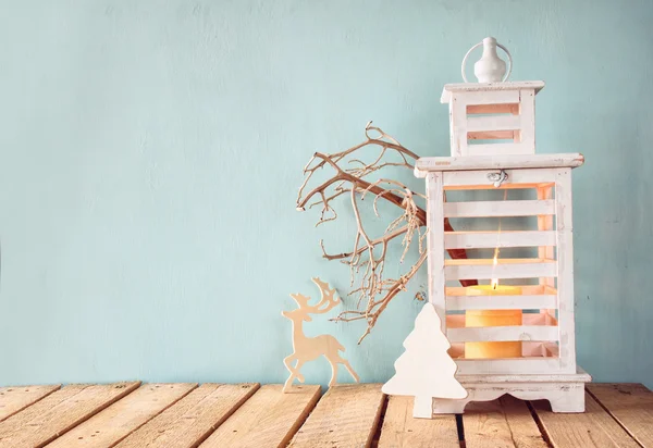 Linterna vintage de madera blanca con vela ardiente, ciervos de madera, regalos de Navidad y ramas de árbol en la mesa de madera . — Foto de Stock