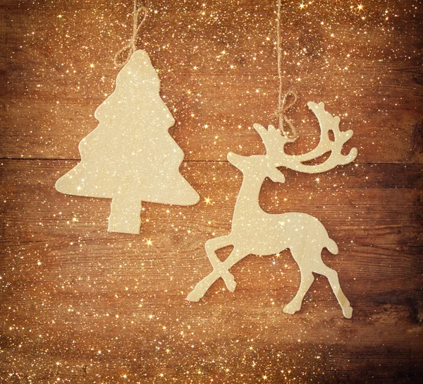Image of wooden decorative christmas tree and reindeer hanging on a rope over wooden background with glitter overlay. — Stock Photo, Image