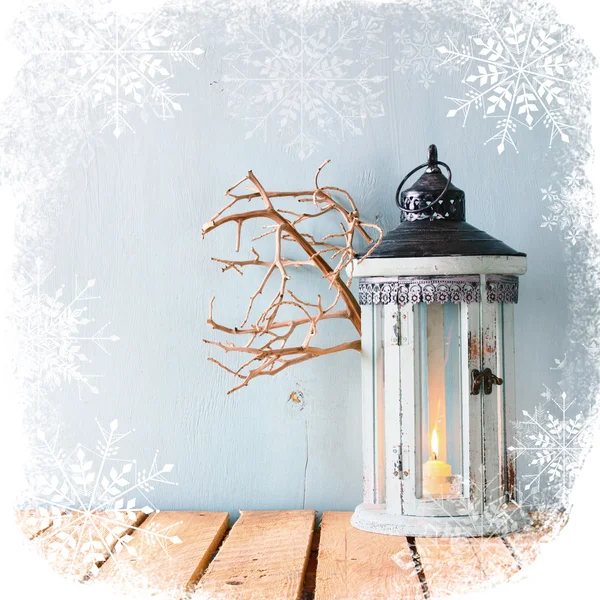 White wooden vintage lantern with burning candle and tree branches on wooden table. retro filtered image snowflake overlay. — Stockfoto