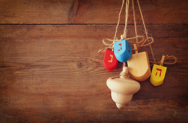 image of jewish holiday Hanukkah with wooden colorful dreidels (spinning top) hanging on a rope over wooden background.