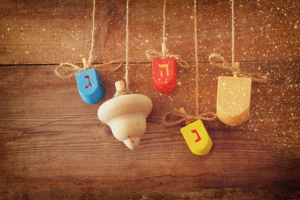 Image of jewish holiday Hanukkah with wooden colorful dreidels (spinning top) hanging on a rope over wooden background. — Stockfoto