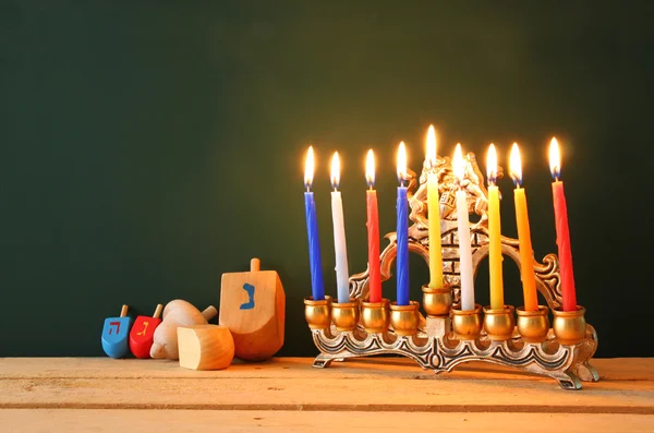 Low key image of jewish holiday Hanukkah with menorah (traditional Candelabra) and wooden dreidels spinning top over chalkboard background, room for text. — Stock Fotó