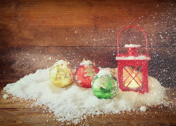 christmas background with red lantern, bauble and snow over wooden background. glitter overlay.