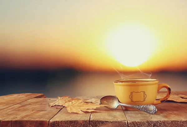 Front image of coffee cup over wooden table in front of lake sunset. — Stock Photo, Image