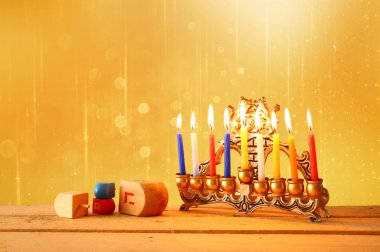 low key image of jewish holiday Hanukkah with menorah (traditional Candelabra) and wooden dreidels (spinning top). glitter background.