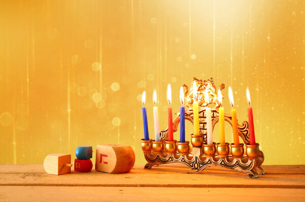 low key image of jewish holiday Hanukkah with menorah (traditional Candelabra) and wooden dreidels (spinning top). glitter background.