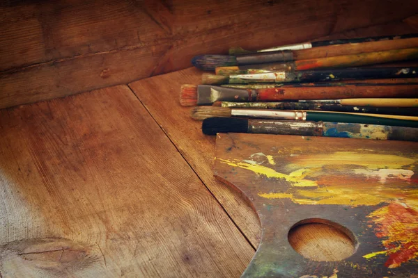 Top view of set of used paint brushes and palette over wooden table. retro filtered image. — ストック写真