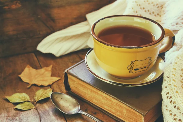 Taza de té con libro viejo, hojas de otoño y una bufanda caliente en la mesa de madera . — Foto de Stock