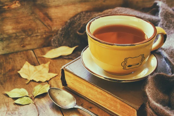Šálek čaje se stará kniha, podzimní listí a teplá šála na dřevěný stůl. — Stock fotografie