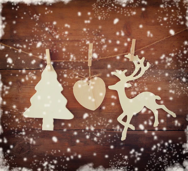 Image of wooden decorative christmas tree and reindeer hanging on a rope over wooden background with abstract snow overlay. — Stock Photo, Image