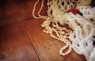 A beautiful natural white pearls and warm scarf on wooden table. retro filtered image.