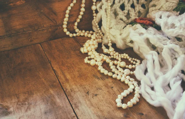 A beautiful natural white pearls and warm scarf on wooden table. retro filtered image.
