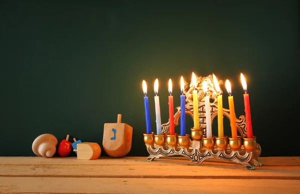 Low key image of jewish holiday Hanukkah with menorah (traditional Candelabra) and wooden dreidels spinning top over chalkboard background, room for text. — 图库照片