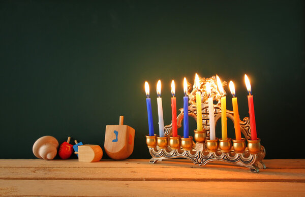 low key image of jewish holiday Hanukkah with menorah (traditional Candelabra) and wooden dreidels spinning top over chalkboard background, room for text.