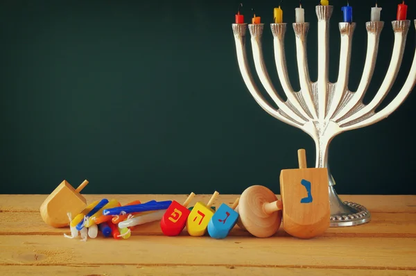 Low key image of jewish holiday Hanukkah with menorah (traditional Candelabra) and wooden dreidels spinning top over chalkboard background, room for text. — Stockfoto