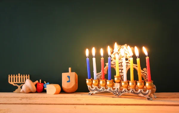 Low key image of jewish holiday Hanukkah with menorah (traditional Candelabra) and wooden dreidels spinning top over chalkboard background, room for text. — 스톡 사진