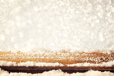 image of wooden old table and december fresh snow on top. in front of glitter background. selective focus.