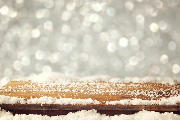image of wooden old table and december fresh snow on top. in front of glitter background. selective focus.