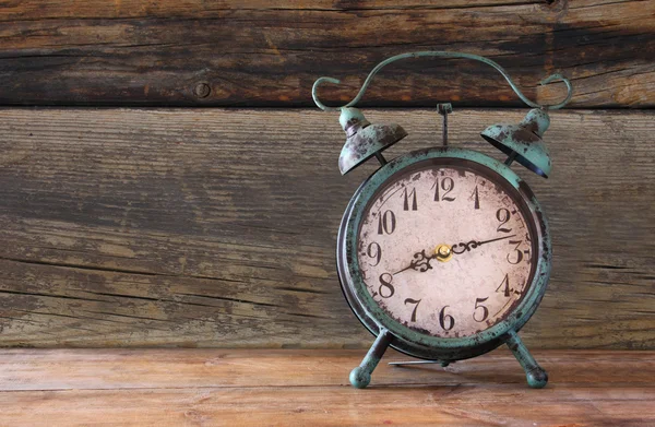 Imagen de reloj despertador vintage sobre mesa de madera delante de fondo de madera. retro filtrado . — Foto de Stock
