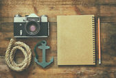 top view image of blank notebook, nautical rope, anchor and camera. travel and adventure concept. retro filtered image.