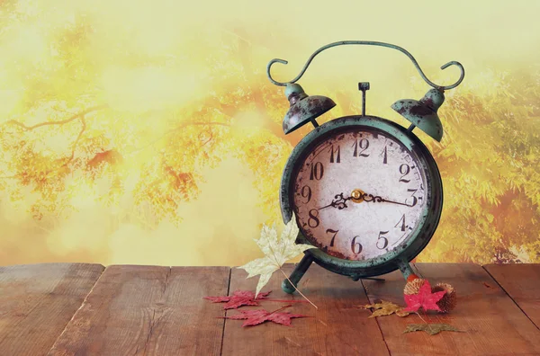 Imagem do relógio de alarme vintage ao lado de folhas de outono na mesa de madeira na frente do fundo embaçado abstrato. retro filtrado . — Fotografia de Stock