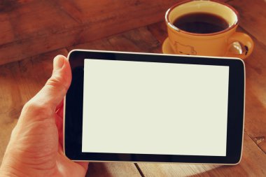 Digital tablet computer with isolated screen in male hands over wooden table background and cup of coffee.