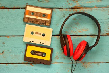 top view of vintage headphones and cassettes over aqua wooden table. retro filtered.
