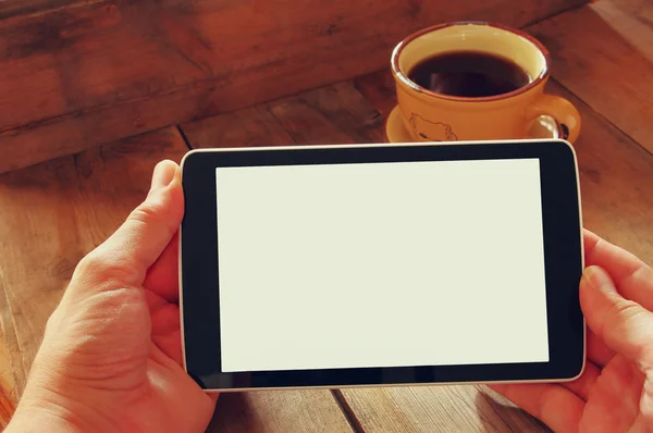 Digital tablet computer with isolated screen in male hands over wooden table background and cup of coffee. — Stok fotoğraf